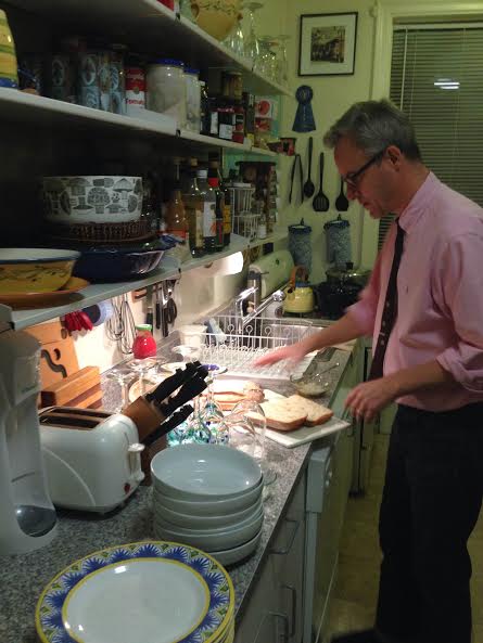 John slathers bread with butter and garlic before it goes in the broiler. Then guests will serve themselves using the plates and pasta bowls stacked on the counter.